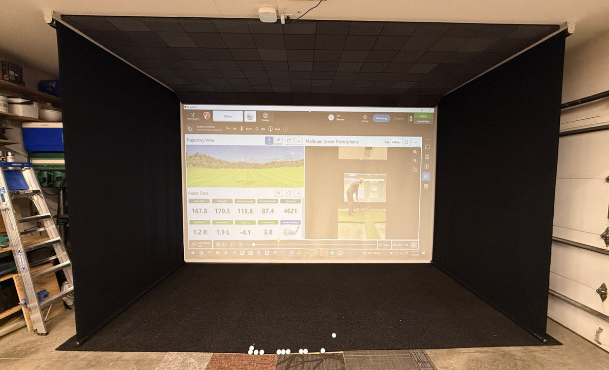 Retractable golf simulator screen with black side walls in a garage