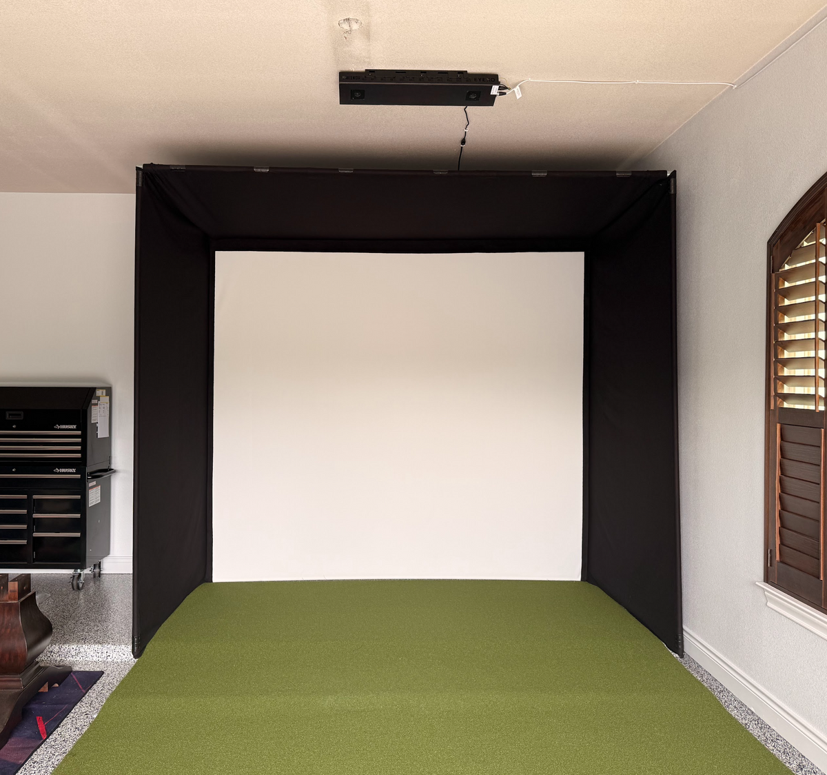 Golf simulator enclosure with an overhead projector and turf floor