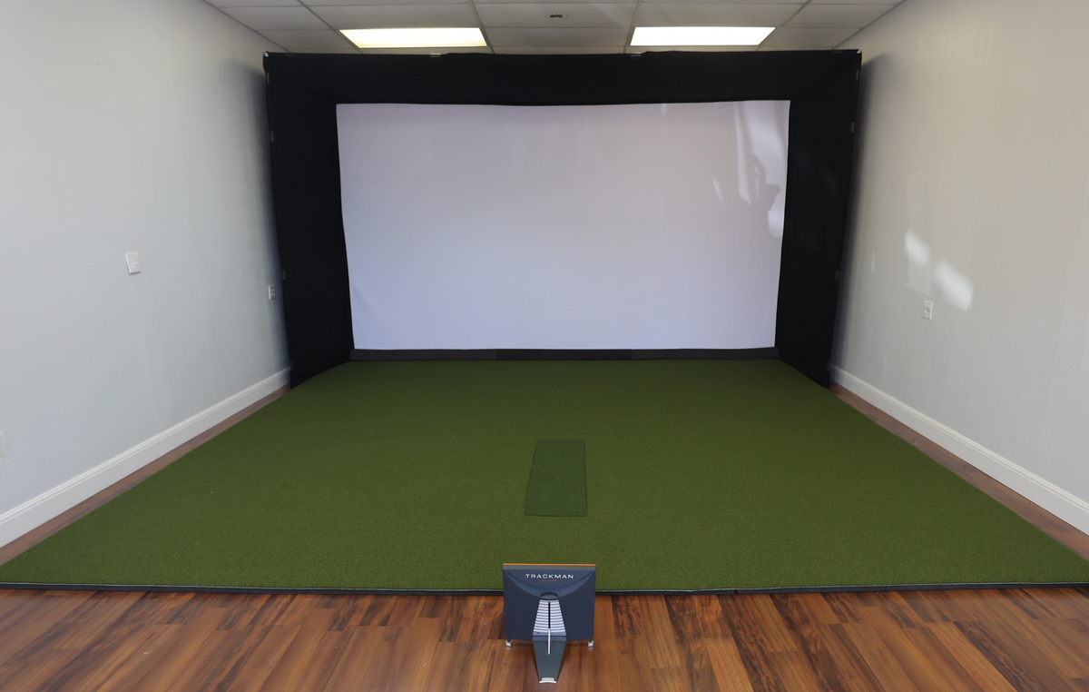Golf simulator enclosure in a spare room with turf and a hitting strip