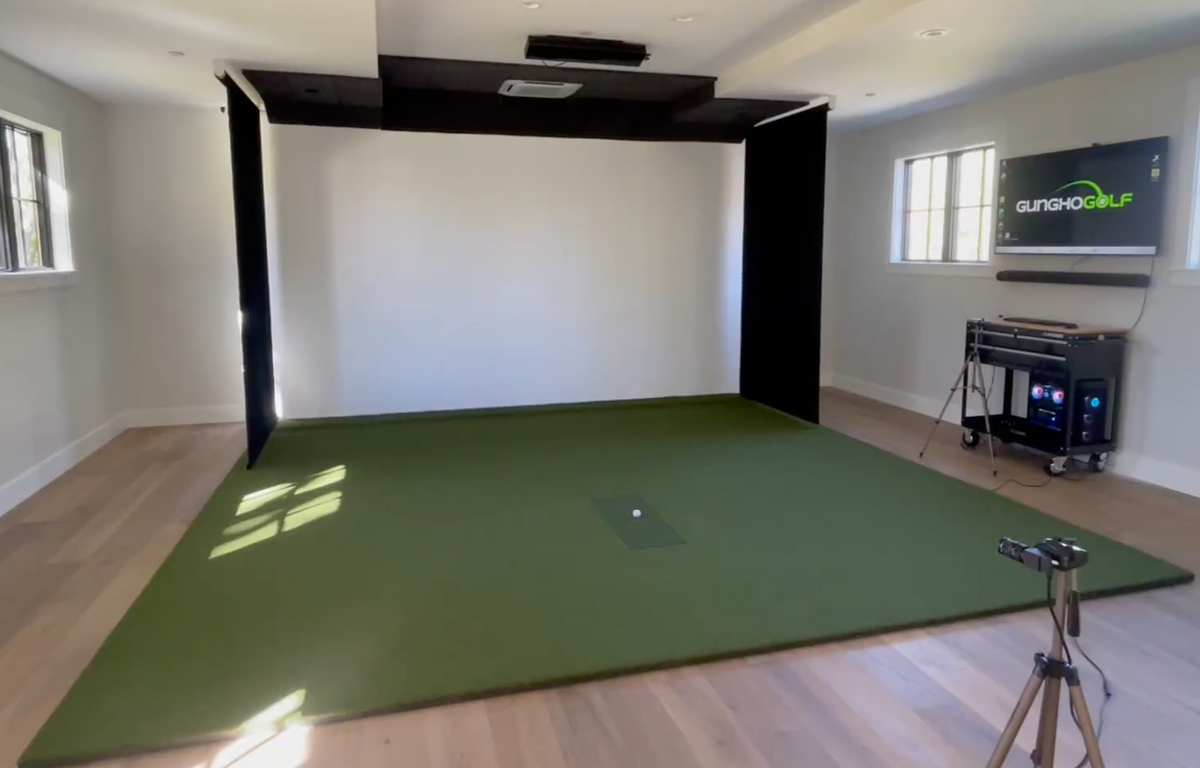 Retractable golf simulator screen in a bright home room with turf and launch monitor